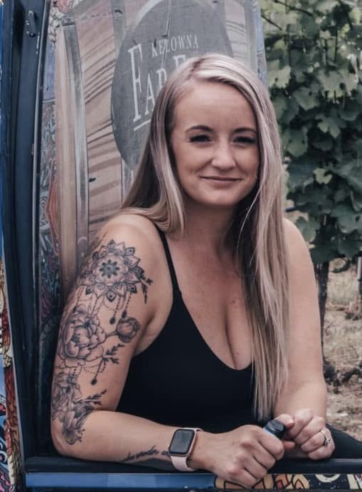 Smiling woman with floral sleeve tattoo in black tank top.
